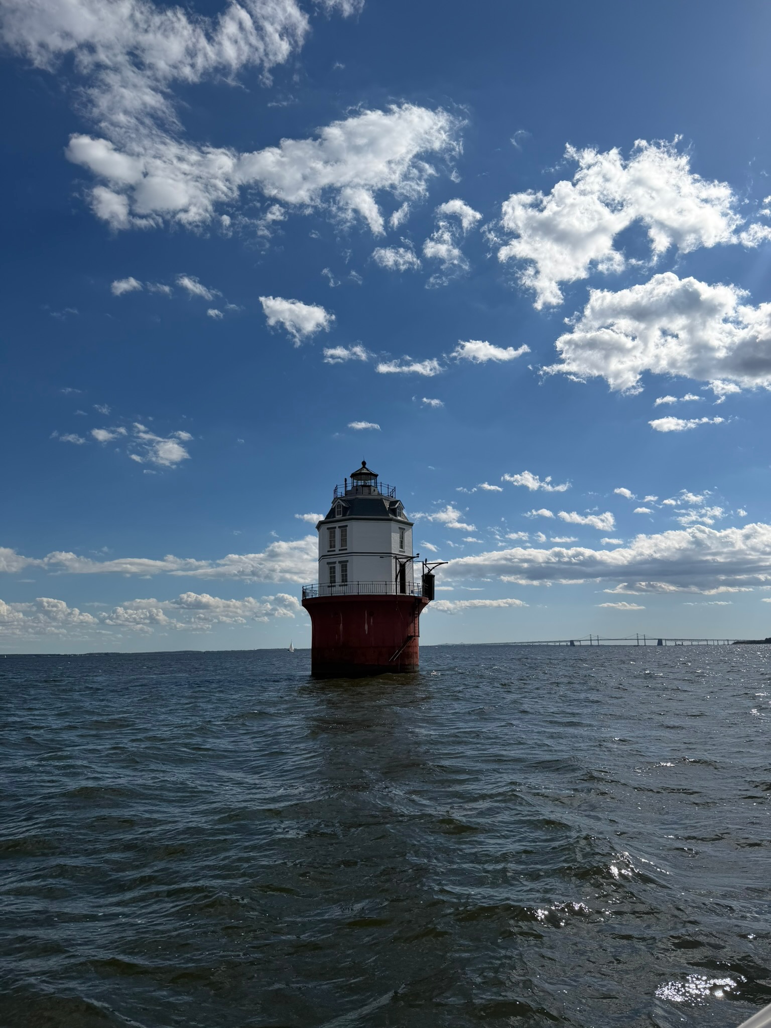 A Chesapeake Bay lighthouse on the open water, with the Bay Bridge in the distance