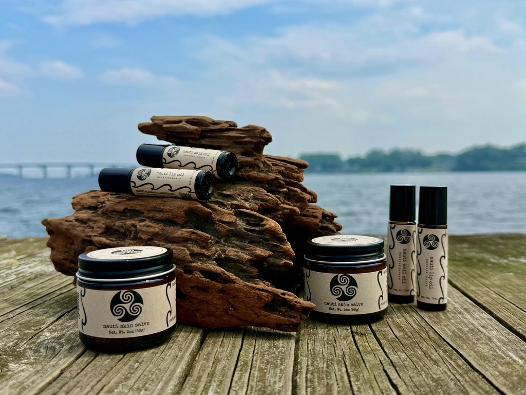 The full nautiskincare line — skin salve, lip oil, and nail oil — together on driftwood by the Chesapeake Bay